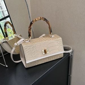 Detail of bamboo handle and beige crocodile embossed texture on luxury crossbody handbag