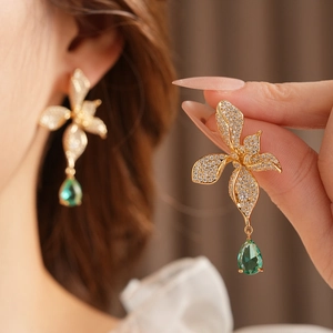 Close-up of golden vintage flower earrings with clear zircon and green teardrop pendant