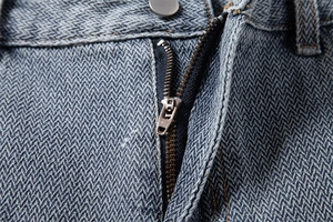 Detailed close-up of metal zipper and herringbone texture on denim shorts