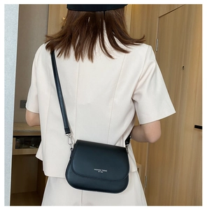 Dettaglio della borsa a sella in pelle nera opaca con testo fashion bianco sulla patta