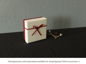 Close-up of gold plated freshwater pearl necklace next to red ribbon gift box
