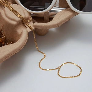 Detail view of a gold pearl chain bracelet with small round metal disc accents on a display
