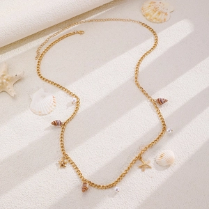 Detail of bohemian gold chain necklace with seashell and starfish pendants on white surface