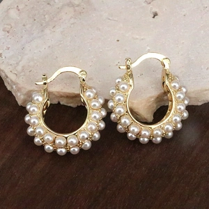 Detailed close-up of golden U-shaped earrings with faux pearl inlay on stone background