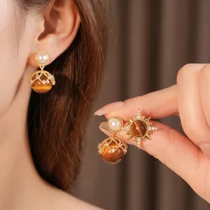 Golden starburst earrings with tiger eye stone and pearls shown on a female model