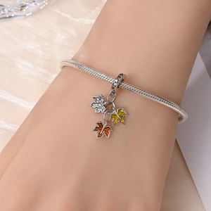 Detail of silver snake chain bracelet featuring yellow and orange enamel maple leaf charms