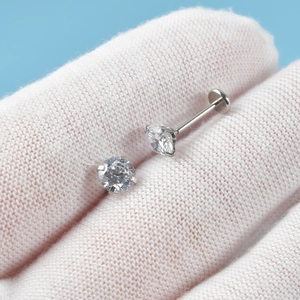 Close-up of silver stainless steel labret studs with round clear zircon on a gloved hand