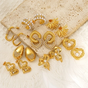 Elegant gold bow and heart stud earrings with pearls on a textured stone surface