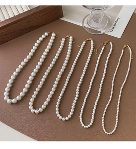 Détail de quatre colliers de perles blanches de tailles variées avec fermoirs dorés