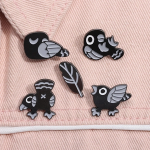Gros plan de cinq épingles émaillées d'oiseaux noirs et plume sur denim rose