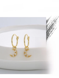 Detail of gold hollow crescent moon earrings with white zircon on a ceramic tray