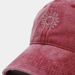 Detailed macro view of white sunflower embroidery on vintage washed red cotton cap fabric