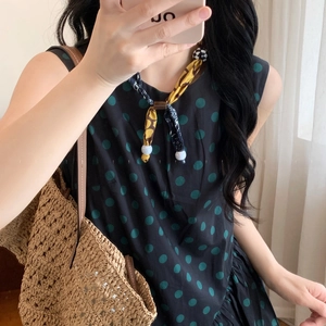 Detail of printed sleeveless dress with green polka dots and yellow scarf accent