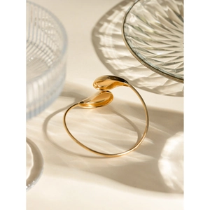 Detailed view of gold stainless steel open bangle with teardrop design on glass