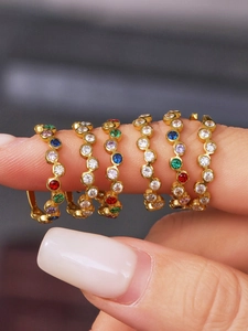 Close-up of six gold-plated rings with colorful cubic zirconia in blue, green, and red