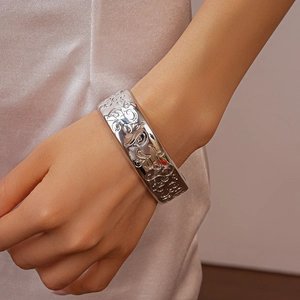 Detail of silver oval open bangle with intricate floral engravings worn on wrist