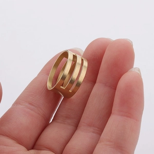 Detail showing a golden brass jump ring opener tool with triple-row hollow design on a finger