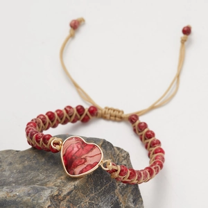 Detail of handmade red stone heart bracelet with gold trim and beige woven cord
