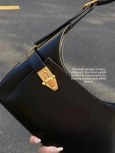 Detail of black leather underarm bag with gold metal lock and side pocket texture