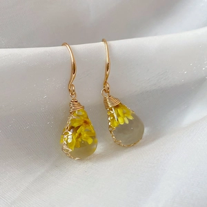 Close-up of handmade teardrop resin earrings with yellow dried flowers and gold wire wrap
