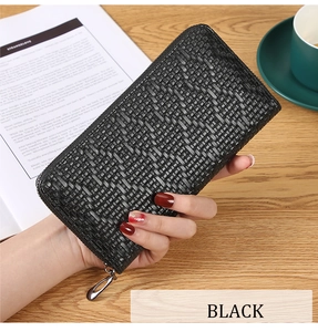 Close-up of black long woven wallet held by a model over a wooden desk background