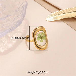 Detail of gold open ring featuring a green dried flower in a clear resin setting