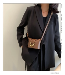 Detail of a brown vintage leather crossbody bag with a gold metal buckle on a model