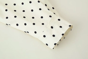Detail of white long sleeve cuff with black polka dots and fine stitching textures