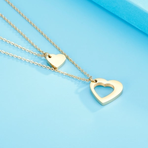Détail d'un collier double rang doré avec pendentif cœur MAMA sur fond bleu clair