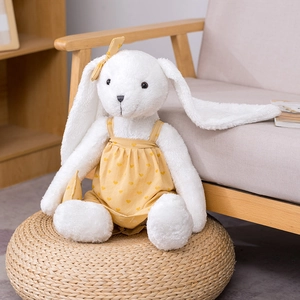 Adorable white plush rabbit in yellow heart overall dress on a woven stool
