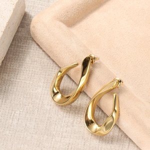 Detailed view of irregular golden twisted hoop earrings on textured stone surface