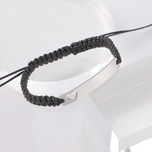 Macro detail of black braided rope bracelet featuring a hollow heart rectangular metal plate