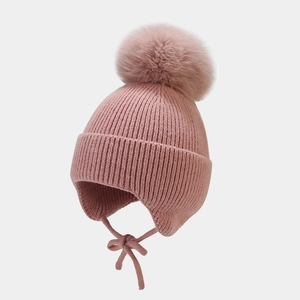 Détail du bonnet en tricot rose avec cache-oreilles, pompon et texture en laine épaisse