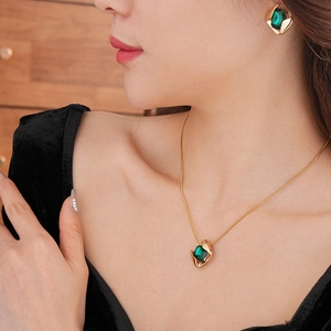 Nahaufnahme des Schmucksets aus Gold mit grünen quadratischen Edelsteinen an einem Model