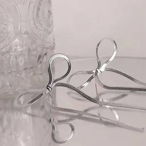 Detail of silver bow tassel earrings featuring sleek snake chains on a mirror surface