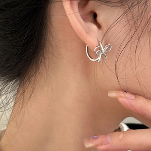 Close-up of elegant silver bow-shaped hoop earrings worn on ear with metallic shine