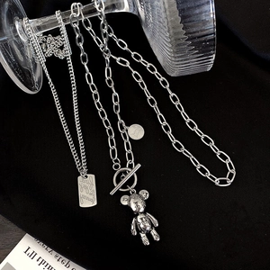 Silver-toned layered necklace set with teddy bear charm and OT buckle on dark fabric