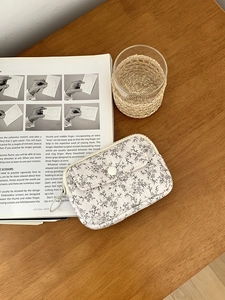 Detailed view of a white floral quilted organizer bag with snap pocket on a wooden desk