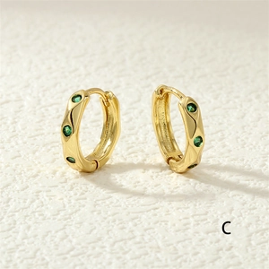 Macro detail of gold hoop earrings featuring green zircon inlay and wavy edge design
