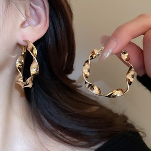 Vue détaillée des boucles d'oreilles créoles dorées avec un design torsadé et métallique
