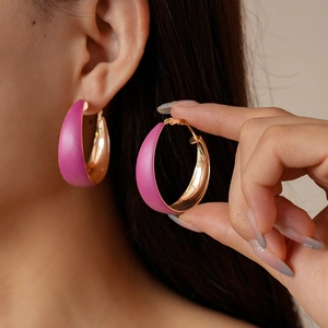 Close-up of magenta enamel chunky C-shaped hoop earrings with gold metal interior