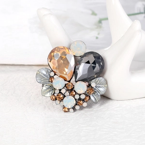 Elegant leaf-shaped crystal brooch with champagne and grey stones on a white hand model
