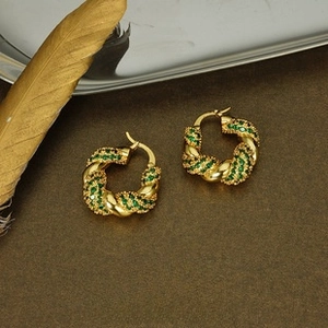 Detail of gold twisted hoop earrings featuring emerald green pavé stones on leather