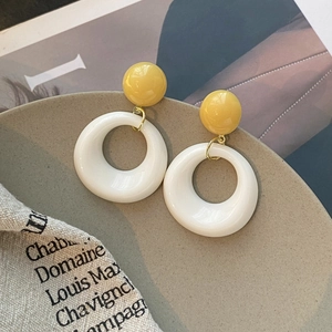 Détail de boucles d'oreilles boules jaunes et cercles blancs sur plateau céramique