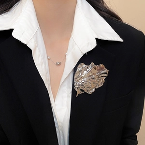 Detailed view of silver pleated leaf brooch on a black suit lapel with pearl necklace
