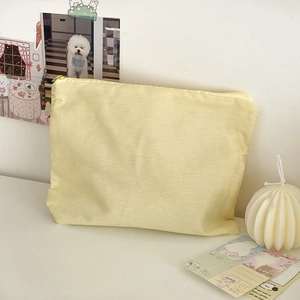 Detail of light yellow plaid fabric cosmetic bag with zipper on a minimalist white desk