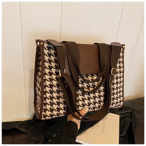 Detailed shot of houndstooth tote bag with brown leather flap held by a model