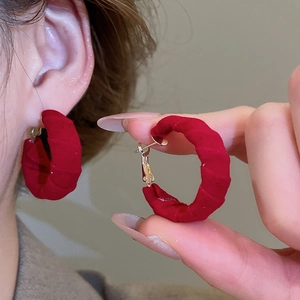 Macro shot of large red velvet twisted hoop earrings with elegant golden metal studs