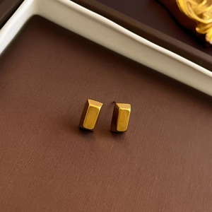 Macro shot of polished gold rectangle stud earrings on a dark textured jewelry box