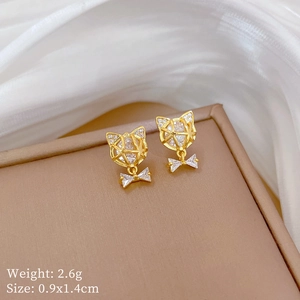 Macro shot of gold cat-shaped earrings with white zircon accents and bow details